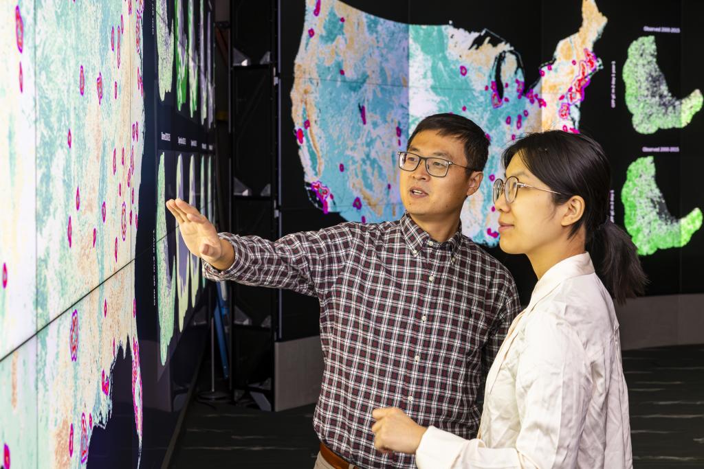 Jiafu Mao, left, and Yaoping Wang discuss their analysis of urban and rural vegetation resilience across the United States in the EVEREST visualization lab at ORNL. Credit: Carlos Jones, ORNL/U.S. Dept. of Energy