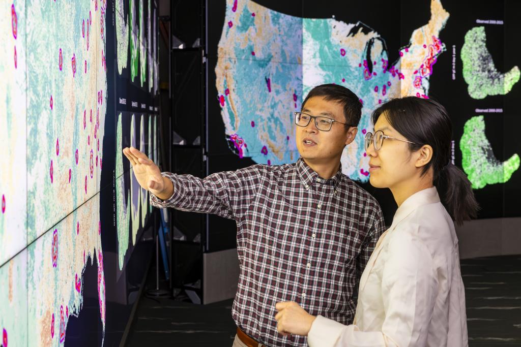 Jiafu Mao, left, and Yaoping Wang discuss their analysis of urban and rural vegetation resilience across the United States in the EVEREST visualization lab at ORNL. Credit: Carlos Jones, ORNL/U.S. Dept. of Energy