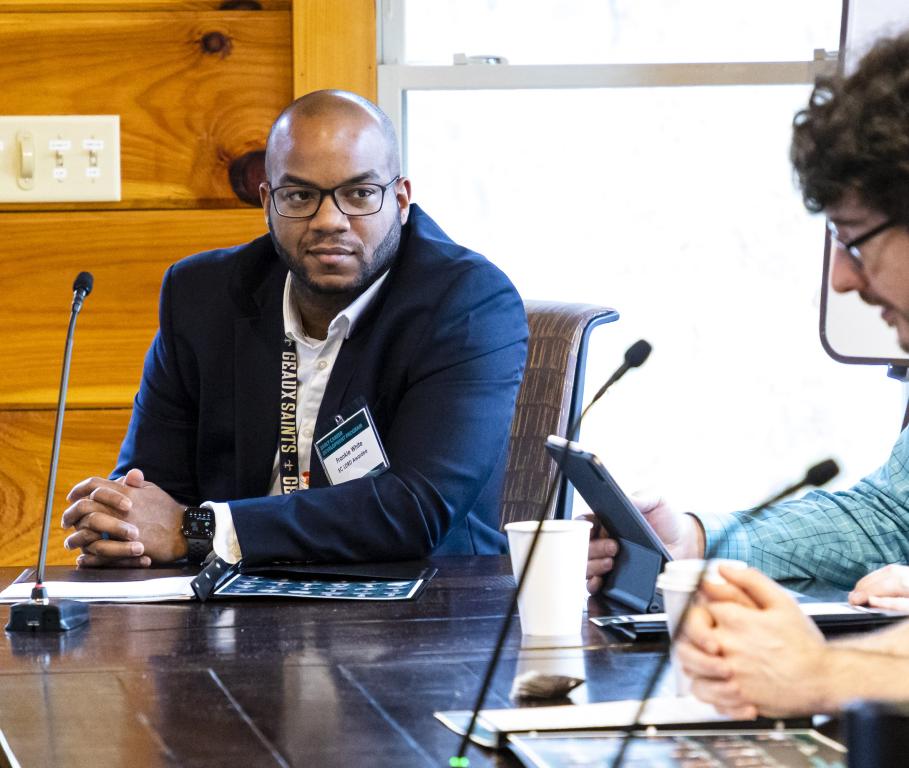 Man sitting at a table, speaking into a microphone to another male at the table