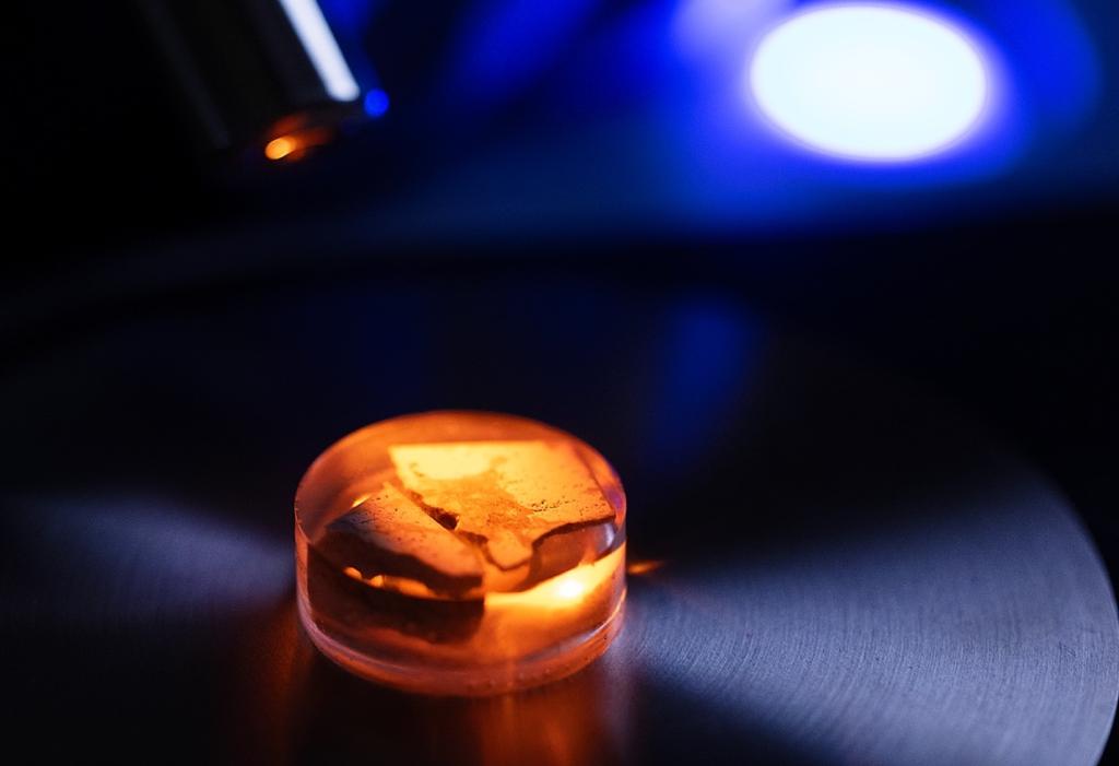 Redish orange sample of material, round in size and small (taking up only a quarter of the image). There is a dark grey floor and blue light background