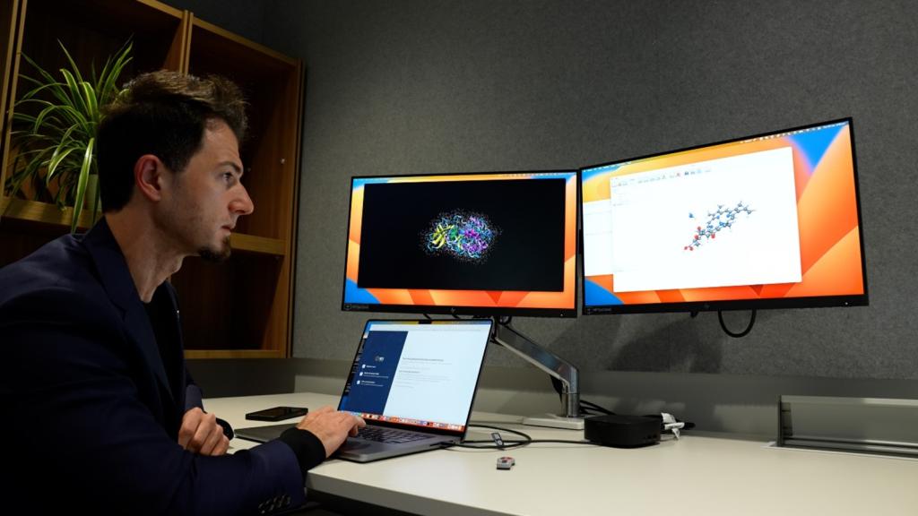 Image of Giuseppe Barca looking at two computer monitors, representing the team using Frontier to perform the first quantum chemistry calculations to exceed an exaflop.
