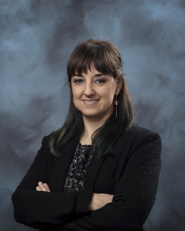Elena Tajuelo Rodriguez is standing with her arms crossed posing for a photo in front of a blue and dark navy background