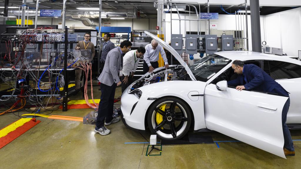 Four scientists are looking at a white car with the hood up and the driver side door open inside the MDF lab