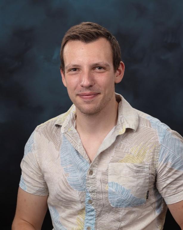Profile photo of man in short sleeve button up shirt with blue and grey feather pattern. 