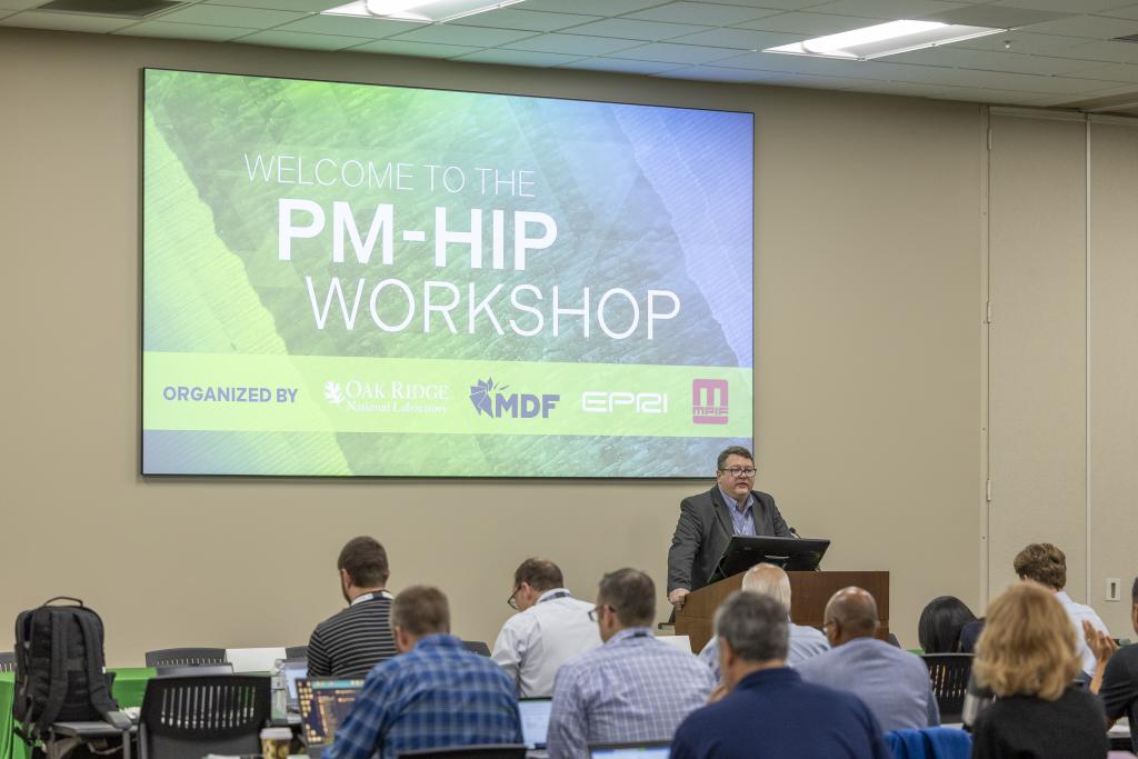 A speaker is standing at the podium in front of a PowerPoint slide with the title of the workshop on it, with 10 people in the audience