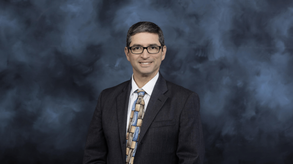 Benjamin Rothrock is pictured, posing in front of a blue and black background in a suit and tie