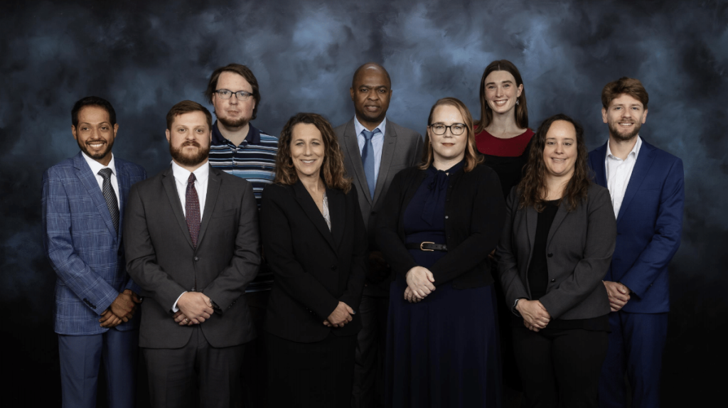 Nine members of the LandScan team are pictured here, posting for a photo in front of a black and blue backdrop