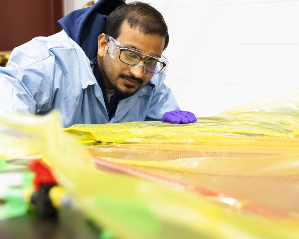 Researcher in blue coat and purple glove is leaning over orange and yellow material.