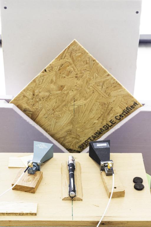 A picture containing table, indoor with a square wooden panel set up vertically to test instruments radar