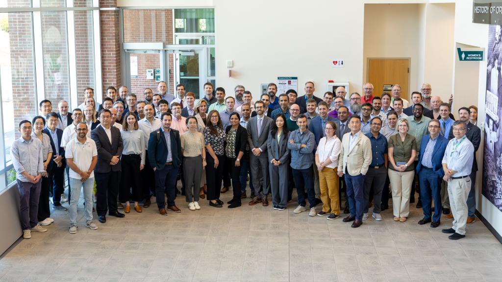 Group photo in the lobby of the conference center, all standing and holding one hand over the other. Sun is shining through the windows
