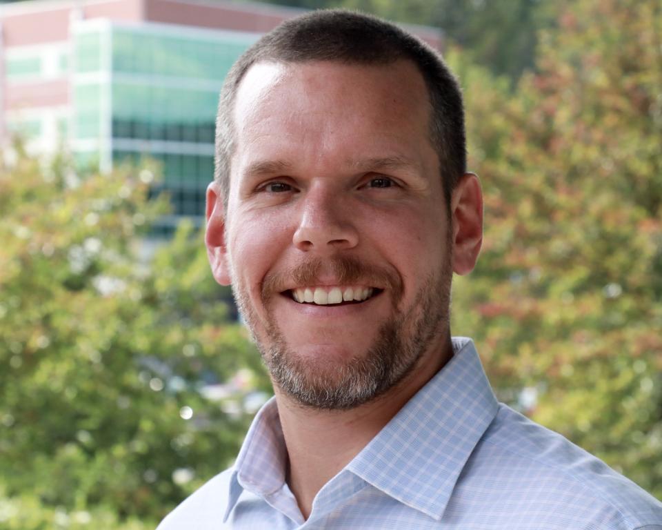 Doug Harris smiles for a photo in a blue button up collared shirt, outside