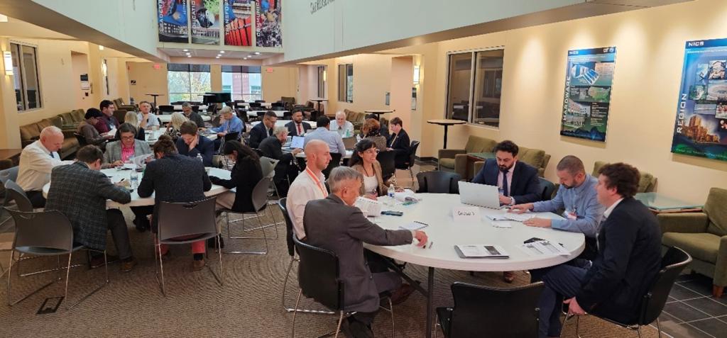 Multiple tables are lined up with six people sitting around each one working on breakout sessions during the workshop event at ORNL