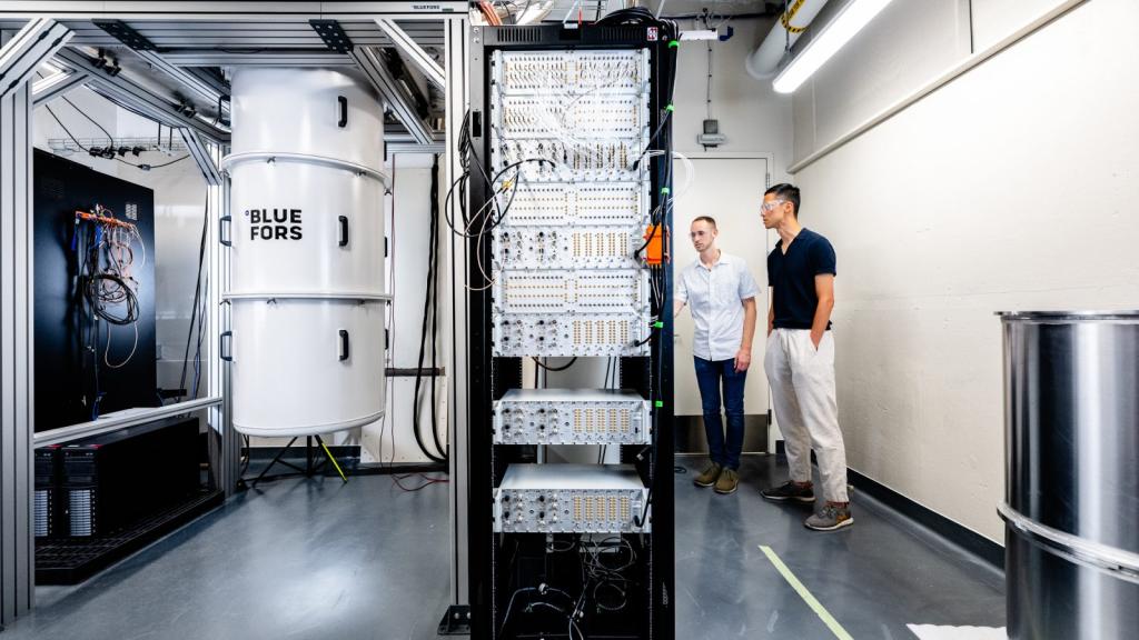 Two collaborators work at the quantum computing test bed, which looks like computers in cabinets