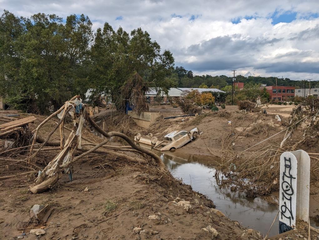 Image shows damage of hurricane with cars in the water, covered in mud and broken trees