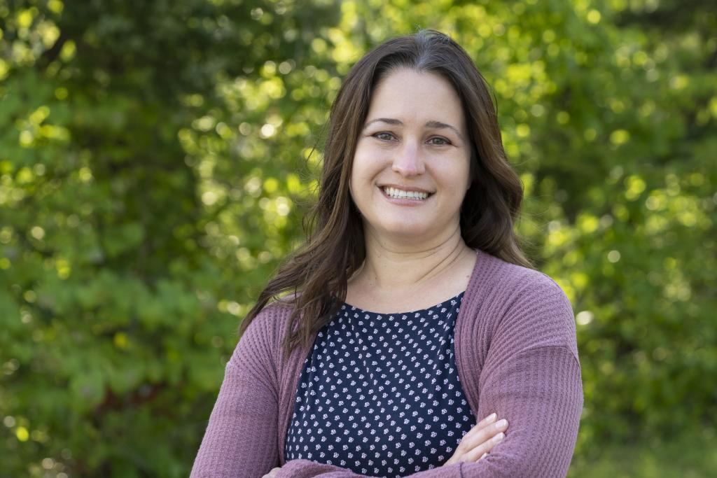 ORNL researcher Melissa Cregger is standing outside smiling for a photo. Woman is wearing blue and white polka dot shirt with a purple cardigan. 