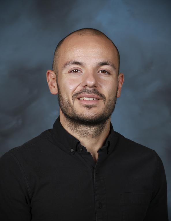 ORNL R&D data scientist Max Pasini is posing for a portrait with a blue background, black button up long sleeve shirt
