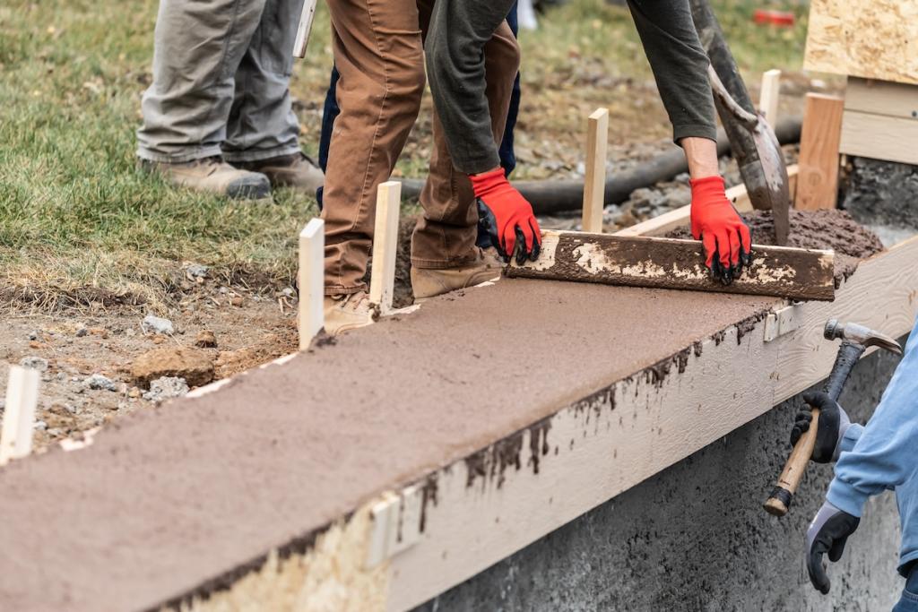 Construction Workers Pouring And Leveling Wet Cement Into Wood Framing. Image from Envato