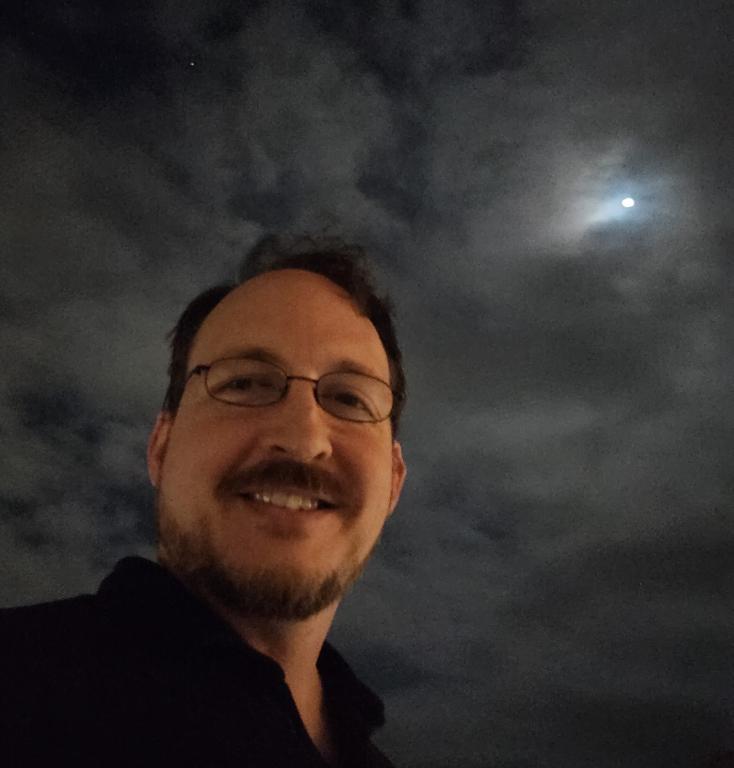 Researcher, Ryan Culler, takes a selfie in glasses under the cloudy night sky