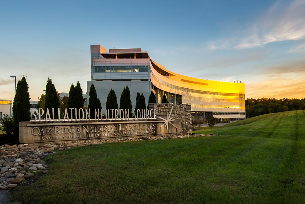 View of the Spallation Neutron Source building and sign out front with blue skies and green grass