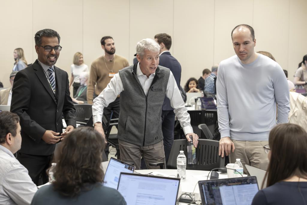 Energy Secretary, CEO for OpenAI and ORNL researcher are standing over a table talking to event participants