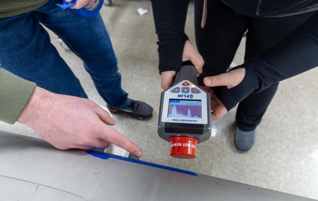 Two researchers are down with their feet and hands only, holding a remote sensor with a red top