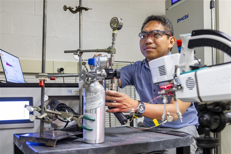 Researcher sitting behind table of equipment fastening a metal tube