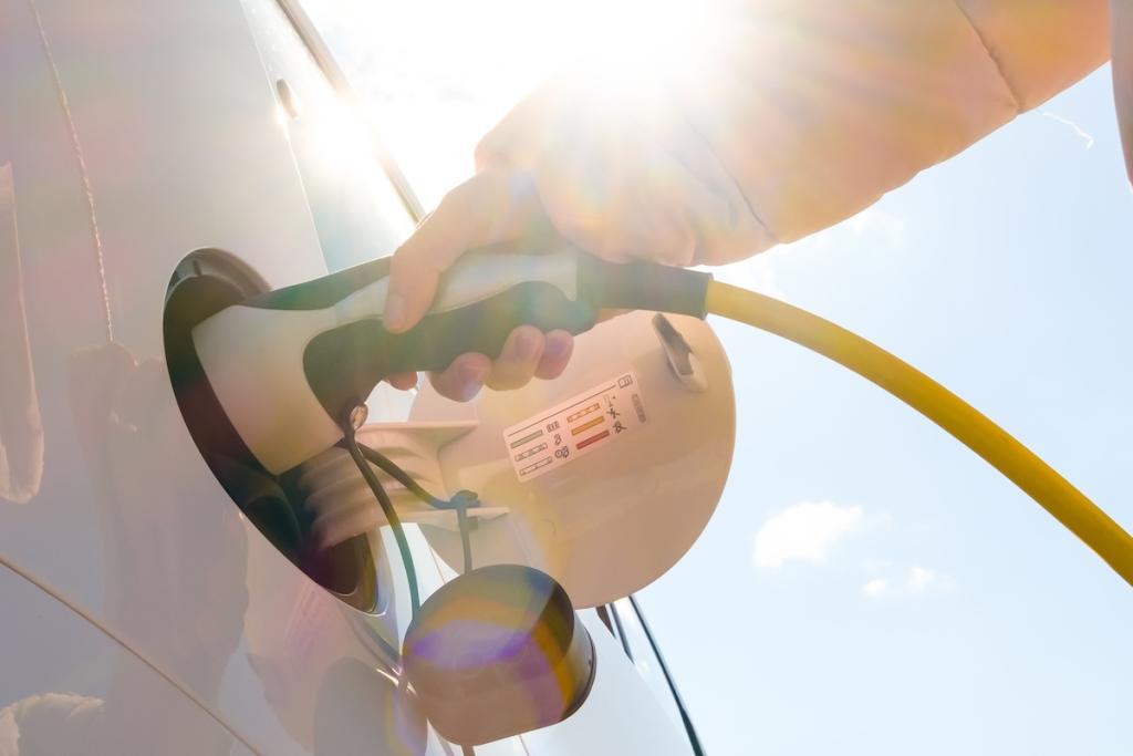 Close up woman hand inserts power cable supply to charge electric or EV car at sunlight. Image from Envato