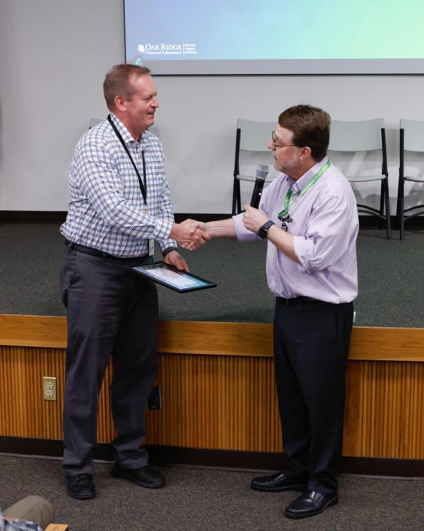 ORNL Director and researcher shake hands as the director presents an award for 40-year career