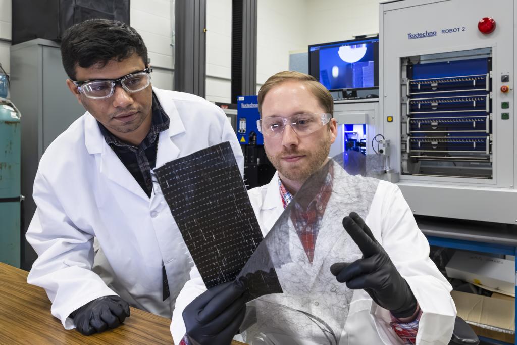 Two ORNL researchers inspect carbon fiber materials - one black rectangular sheet and one see-through sheet of film.