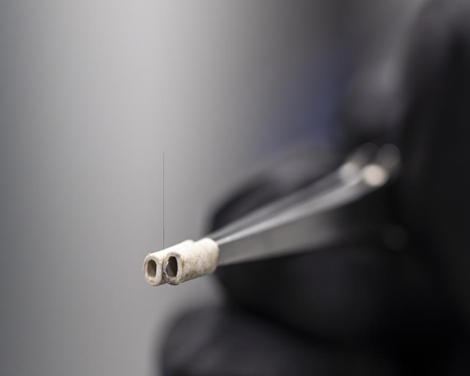 A close-up photo of carbon fiber that is being held on a pair of tweezers.