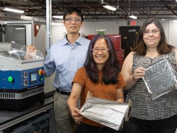 Three researchers are standing in the lab holding a film that they created.