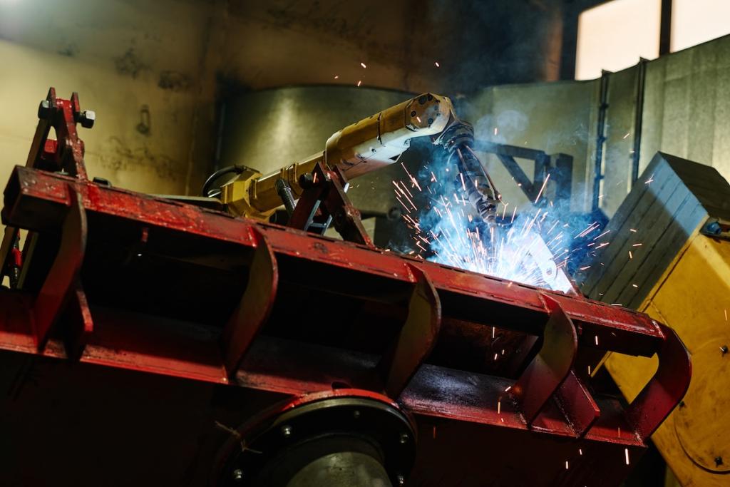 Close-up of automated welding machine at work in an industrial environment, producing sparks and bright flashes. Machinery is set against a background of metal structures and equipment. Image from Envato