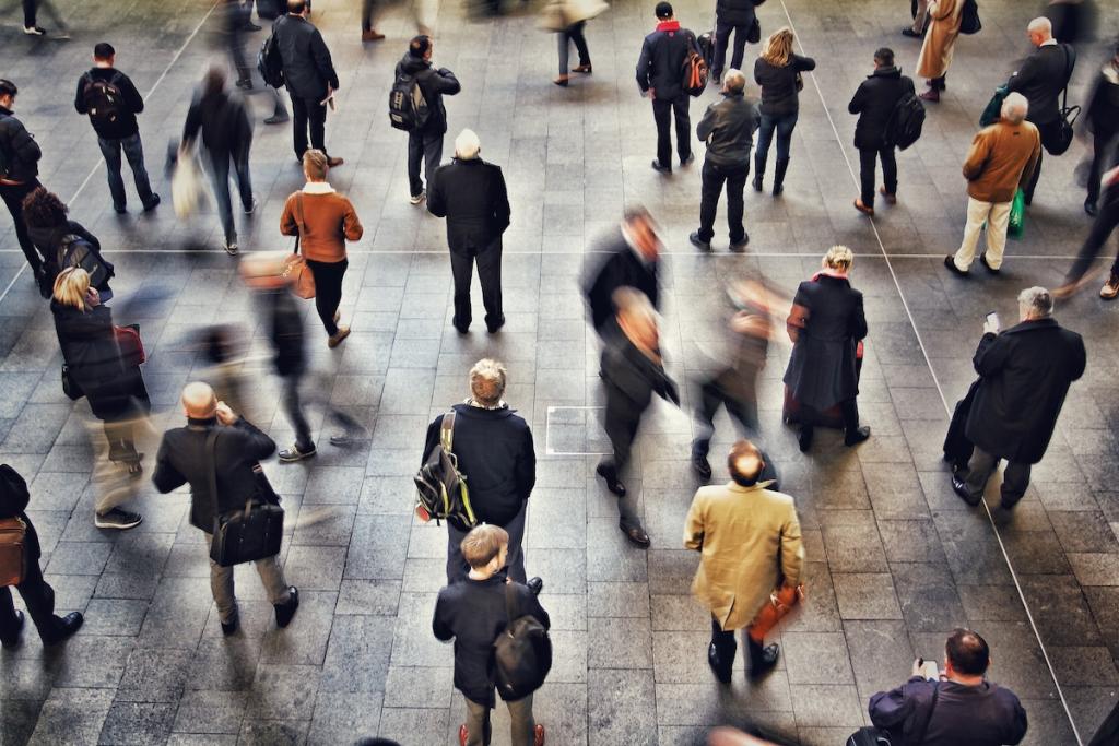 Commuters, passengers and travellers standing and waiting for their trains on a busy train station concourse. Blurred motion. Image from Envato.