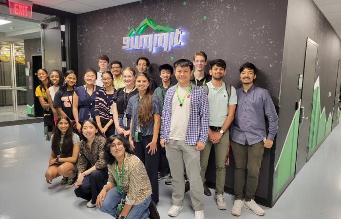 Group of NEXTGENCOMPUTING students in front of the Summit Supercomputer with a green summit mountain logo