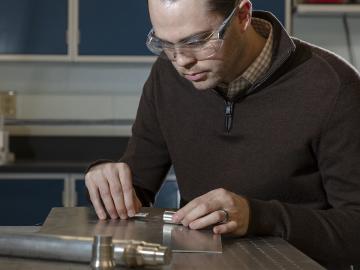 Oak Ridge National Laboratory’s Chris Petrie assembles a fiber optic sensor, fabricated using additive manufacturing, for measuring dimensional changes. Petrie is developing fiber optic–based sensors that can offer greater insights into how materials, such as fuel cladding, perform during irradiation testing inside ORNL’s High Flux Isotope Reactor. Credit: Carlos Jones/Oak Ridge National Laboratory, U.S. Dept. of Energy