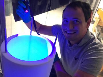 SCGSR Awardee Jacob Zettlemoyer, Indiana University Bloomington, led data analysis and worked with ORNL’s Mike Febbraro on coatings, shown under blue light, to shift argon light to visible wavelengths to boost detection. Credit: Rex Tayloe/Indiana University