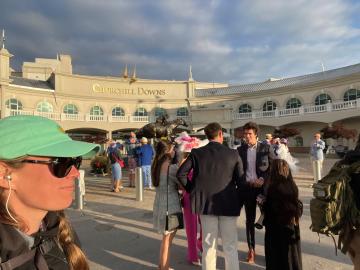 Angie Lousteau, wearing a green hat and sunglasses, takes a selfie outside of the Churchill Downs at the Kentucky Derby. 