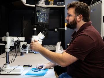 Alex Mullins, a cyber security technical professional at ORNL, deciphers microscopic markings on each chip on a board. Credit: Genevieve Martin/ORNL, U.S. Dept. of Energy