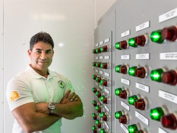 A man stands with arms crossed next to an energy system control panel