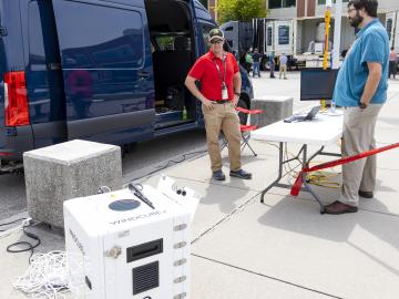 Erik Kabela, in red, demonstrates the wind cube, a piece of equipment that uses light to read weather data. Credit: Carlos Jones/ORNL, U.S. Dept. of Energy