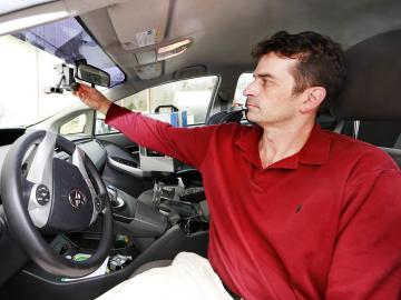 Tom Karnowski sits in the drivers seat of a car and adjusts a sensor behind the rear view mirror