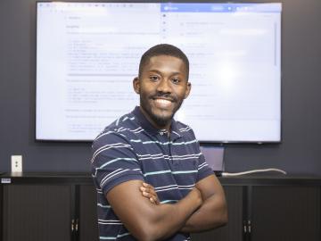 Joel stands in front of a screen with computer code displayed