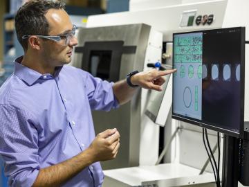 ORNL researcher Zackary Snow compares data from different types of images collected during and after metal parts were additively manufactured using a powder bed printer like the one behind him. Credit: Carlos Jones/ORNL, U.S. Dept. of Energy 