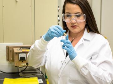 ORNL’s Tyler Spano examines a sample of uranyl nitrate solution that she uses as a precursor to many uranium oxide syntheses. Credit: Carlos Jones/ORNL, U.S. Dept. of Energy