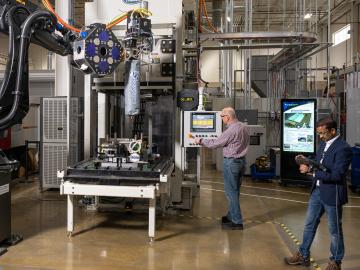 ORNL Composites Innovation staff members David Nuttall, left, and Vipin Kumar use additive manufacturing compression molding to produce a composite-based finished part in minutes. AMCM technology could accelerate decarbonization of the automobile and aerospace industries. Credit: ORNL, U.S. Dept. of Energy