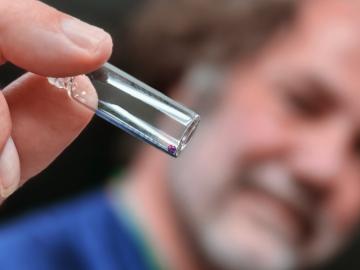 Man in a beard holding tweezers, showing a bead if space glass closer to the screen.  