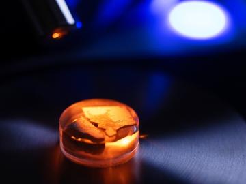Redish orange sample of material, round in size and small (taking up only a quarter of the image). There is a dark grey floor and blue light background