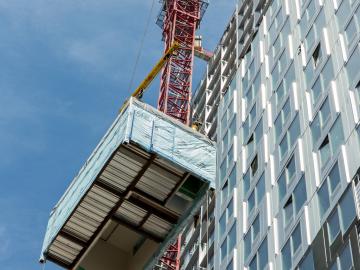 Rectangular box being lifted by a red pully system up the left side of the building