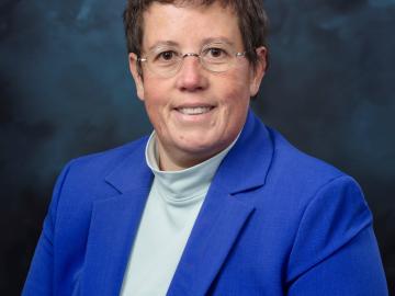 woman in blue blazer, glasses and short hair smiles for a portrait.