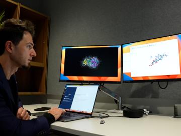 This is an image of a man sitting at a computer with three screens.
